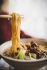 Ciotola di primo piano di deliziosa zuppa di spaghetti asiatici con costolette di maiale poste sul tavolo del caffè — Foto stock