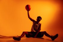 Femme noire avec tenue de basket en studio en utilisant des gels de couleur et des projecteurs sur fond orange — Photo de stock