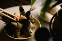 Открытые и покрытые бамбуковые листья риса пельмени помещены на милую клетчатую тарелку с палочками сверху — стоковое фото