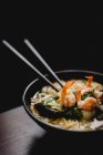 Tigela de saborosa sopa de macarrão oriental com camarões frescos colocados na mesa contra fundo preto — Fotografia de Stock