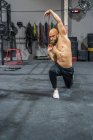 Plein corps sans chemise barbu gars regardant loin étirement élastique bande avec les bras et de fente pendant l'entraînement fonctionnel dans la salle de gym — Photo de stock