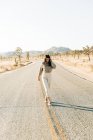 Full body of brunette walking down empty roadway in hot terrain of Joshua Tree National Park in California USA — Stock Photo