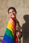 Contenido joven bisexual étnica femenina con bandera multicolor que representa símbolos LGBTQ mirando a la cámara en un día soleado - foto de stock