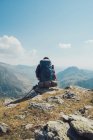 Back view of unrecognizable traveling man sitting resting during hiking in mountains with trekking pole during vacation in summer in Wales — Stock Photo
