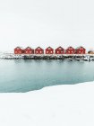 Red cabins and snowy quay located near rippling sea on cold winter day in coastal village on Lofoten Islands, Norway — Stock Photo