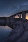 Удивительный пейзаж старого каменного моста с арочными элементами, пересекающими реку под вечерним небом с светящимся Млечным Путем и солнечным светом — стоковое фото