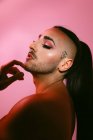 Side view portrait of glamorous transgender bearded woman in sophisticated make up posing against pink background at studio — Stock Photo