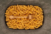 Top view of gold fork placed near uncooked fusilli pasta on tray on table — Stock Photo