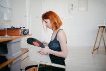 Giovane donna che seleziona il disco in vinile dal contenitore di legno mentre siede contro il giradischi vintage nella stanza della casa — Foto stock