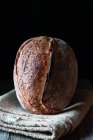 Rustic homemade fresh sourdough rye loaf on blanket in black background — Stock Photo