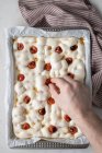 Сверху анонимный человек украшает тесто для вкусной фокаччи сушеными помидорами — стоковое фото