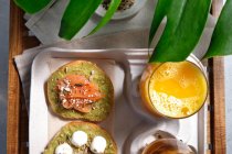 From above of delicious avocado toasts with salmon and burrata cheese served on table with glasses of fresh juice and herbal tea placed near exotic Monstera deliciosa plant — Stock Photo