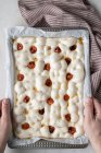 Сверху анонимный человек украшает тесто для вкусной фокаччи сушеными помидорами — стоковое фото