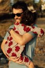 Side view of adult man in sunglasses carrying and embracing girl with closed eyes on weekend day in countryside — Stock Photo