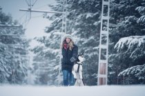 Домашняя собака бегает с женщиной между деревьями в зимнем лесу — стоковое фото