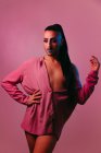 Portrait of glamorous transgender bearded woman in sophisticated make up posing with hands on waist against pink background at studio looking away — Stock Photo