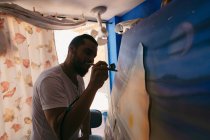 Vista laterale di artista maschile utilizzando pistola a spruzzo per dipingere quadro su tela durante il lavoro in laboratorio creativo — Foto stock