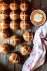 From above hand with appetizing freshly baked sourdough hot cross buns and mug of coffee on wooden table — Stock Photo