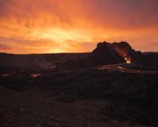 Pintoresca vista del volcán activo con lava caliente situado contra el cielo nublado al atardecer en Islandia - foto de stock