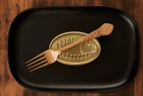 Top view of golden fork placed near sealed canned food on rectangular black tray — Stock Photo