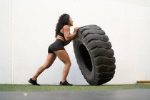 Visão lateral do atleta feminino asiático muscular lançando pneu pesado durante o treinamento intenso — Fotografia de Stock