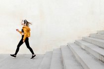 Молода атлетична біла жінка в навушниках і спортивному вбранні, бігає по сходах на відкритому повітрі — стокове фото