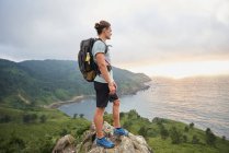 Side view of male traveler standing on rock and admiring view of sea during trekking in summer — Stock Photo