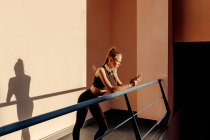 Young woman leaning on banister and relaxing using phone after working out outdoors at sunset — Stock Photo