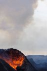 Спалахи гарячої оранжевої лави вивергаються з вулканічної вершини в оточенні диму в Ісландії. — стокове фото