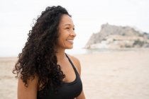 Athlète féminine asiatique positive aux cheveux bouclés riant sur le bord de mer sablonneux en été — Photo de stock
