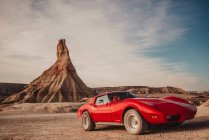 Auto sportiva rossa di lusso parcheggiata vicino alla vetta della montagna contro il cielo nuvoloso nel deserto del Parco Naturale Bardenas Reales in Navarra, Spagna — Foto stock