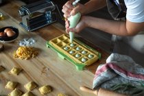 Personne méconnaissable préparant des raviolis et des pâtes à la maison. Elle remplit les raviolis avec un sac à pâtisserie. — Photo de stock