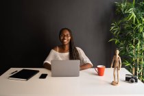Веселая афроамериканка-фрилансер, сидящая за столом на современном рабочем месте, работая над проектом вдали от дома — стоковое фото