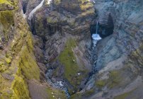 Do córrego acima da água limpa que cai de penhascos pedregosos ásperos cobertos do musgo no campo de Islândia — Fotografia de Stock