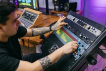 Side view of crop tattooed male sound engineer working with control panel on audio board in recording studio — Stock Photo