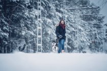 Домашняя собака бегает с женщиной между деревьями в зимнем лесу — стоковое фото
