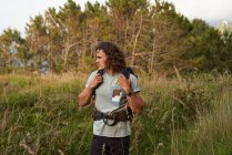 Zaino in spalla maschile passeggiando nel prato al tramonto durante il trekking in estate e guardando altrove — Foto stock