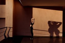 Junge athletische kaukasische Frau hört Musik und dehnt sich bei Sonnenuntergang, Schatten und Licht im Hintergrund — Stockfoto