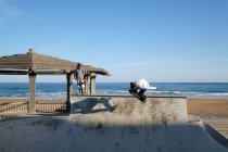 Активные скейтбордисты летом катаются на скейтбордах и демонстрируют трюки в скейт-парке на берегу моря — стоковое фото