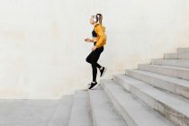 Young athletic caucasian woman wearing headphones and sport outfit, running on stairs outdoors — Stock Photo