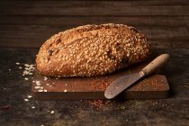 From above of appetizing crispy freshly baked homemade bread loaf with oatmeal flakes and raisin placed with knife on wooden cutting board — Stock Photo