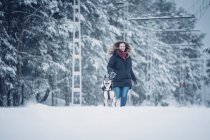 Beautiful domestic hunter dog running with woman between trees in winter forest — Stock Photo