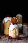 Vários deliciosos kulichs caseiros vertidos com esmalte doce e decorados com pedaços de laranja seca e flores na mesa de madeira — Fotografia de Stock