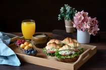 Délicieux croissants sandwichs aux légumes servis sur plateau avec cappuccino et jus d'orange préparés pour le petit déjeuner français et placés sur une table en bois — Photo de stock