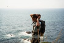 Mochilero masculino caminando en la colina durante el trekking en verano y mirando hacia otro lado - foto de stock