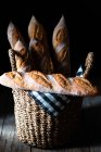 Несколько свежеиспеченных вкусных французских багетов в плетеной корзине с салфеткой на деревянном столе — стоковое фото