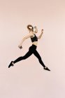 Junge athletische kaukasische Frau mit Kopfhörern und Sportkleidung springt vor hellem Hintergrund im Freien — Stockfoto