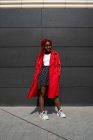 Ganzkörper-Afroamerikanerin mit Brille, die Hände in Manteltaschen vor grauer Wand — Stockfoto