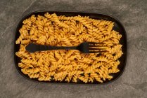 Top view of black fork placed near uncooked fusilli pasta on tray on table — Stock Photo