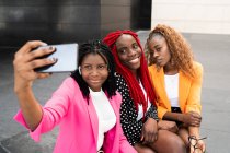 Високий кут друзів афроамериканців, які сидять близько і фотографують на мобільному телефоні. — стокове фото